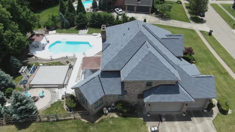 Aerial view of gray shingle roof on stone house with pool