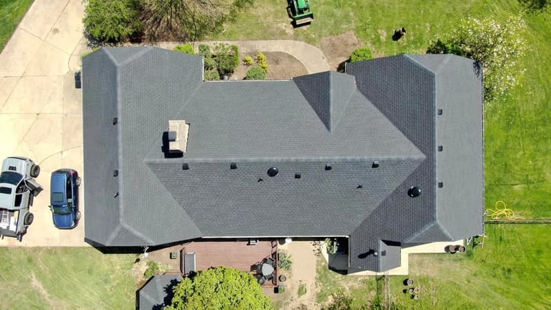 Top-down view of dark shingle roof with vehicles nearby
